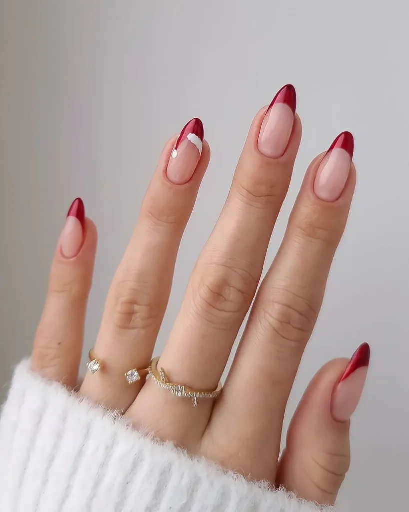 Red French tip Christmas nail designs with glossy burgundy tips, a sheer pink base, and a delicate white accent on almond-shaped nails.