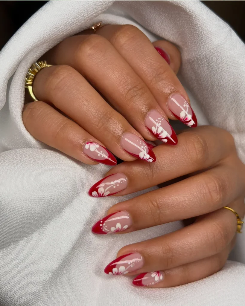 Red French Tips With Snowy White Swirls featuring nude-pink nails, glossy red tips, and delicate white floral nail art.
