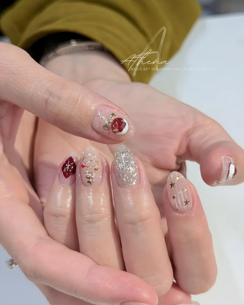 Short Christmas press on nail designs with a sheer pink base, red glitter accents, silver sparkle, tiny gold stars, and festive Christmas ornaments.