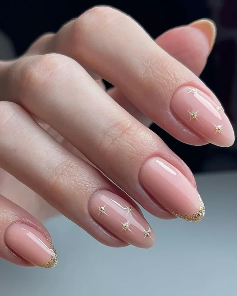 Short french tip christmas nail designs featuring glossy blush-pink almond nails, delicate gold glitter French tips, and tiny gold starburst accents, inspired by elegant white french tip christmas nail designs.