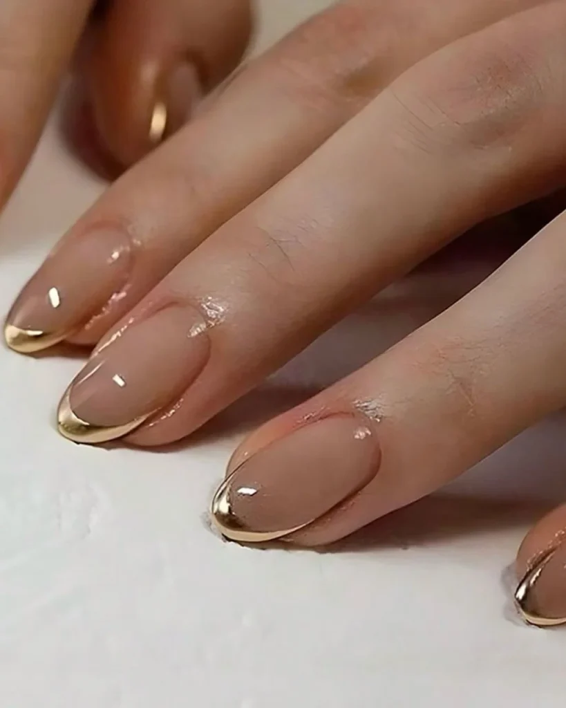 Short french tip christmas nail designs featuring glossy nude pink nails with elegant metallic gold French tips.