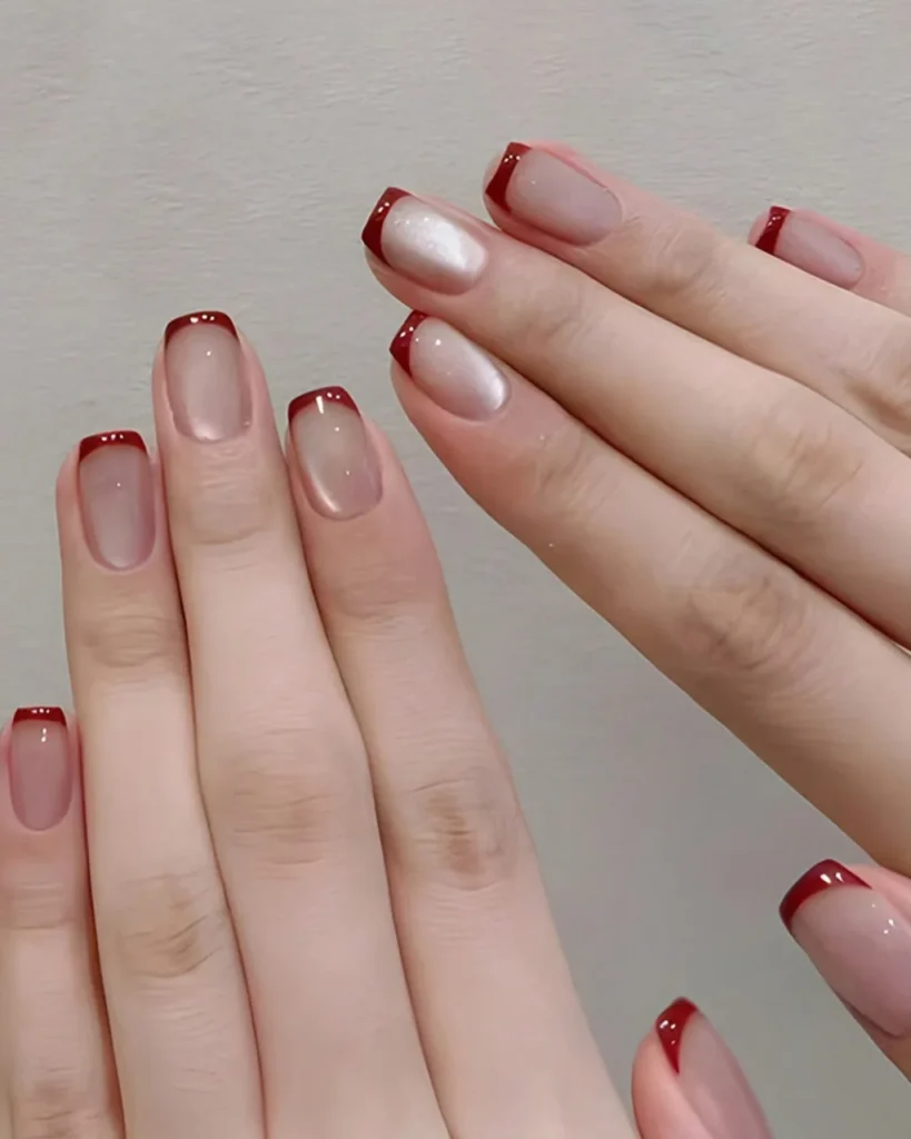 Short french tip christmas nail designs featuring glossy nude pink nails with deep red French tips on short square-shaped nails.