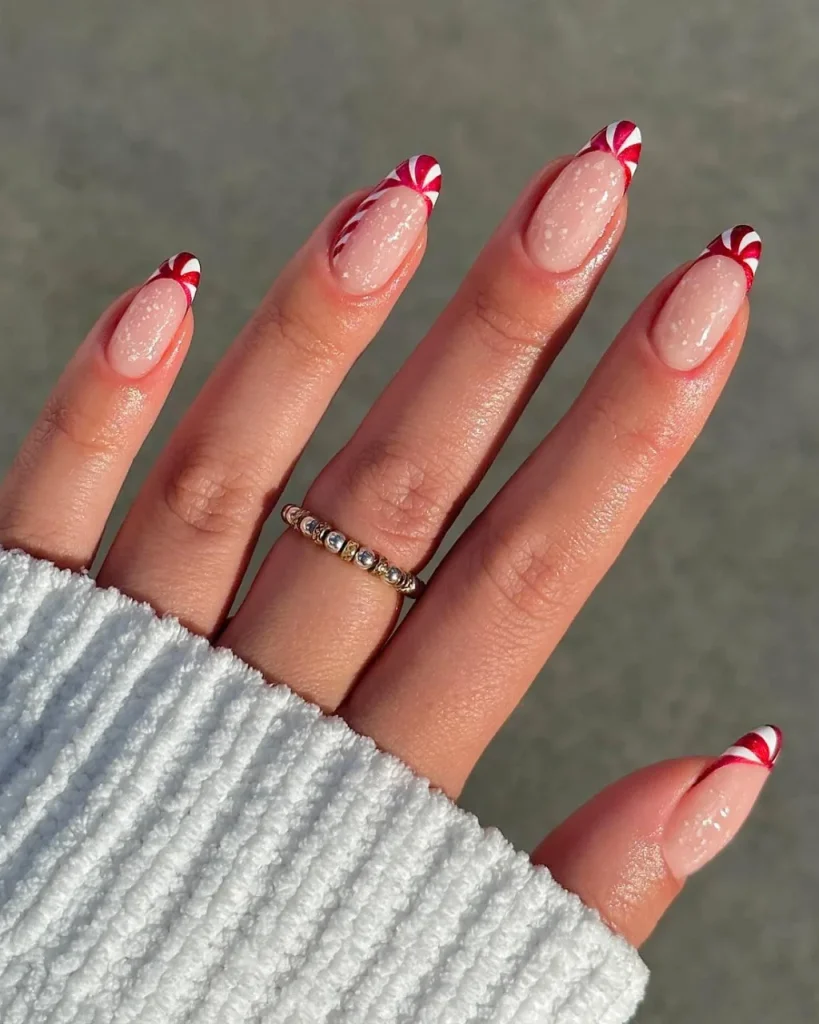Short french tip christmas nail designs with red and white candy cane French tips, featured as a festive variation of white french tip christmas nail designs on nude pink almond nails with subtle glitter
