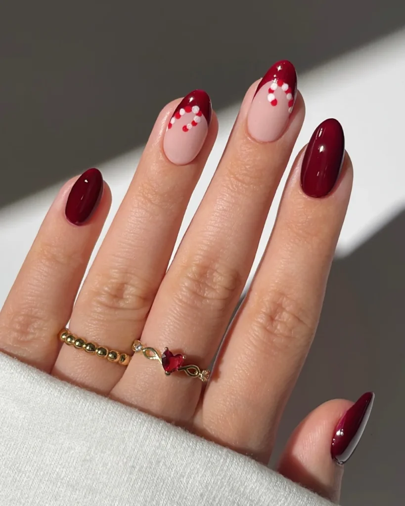Short french tip christmas nail designs featuring blush-pink nails with burgundy and white French tip accents, tiny red and white dots, and glossy deep burgundy accent nails, offering a festive twist on white french tip christmas nail designs.