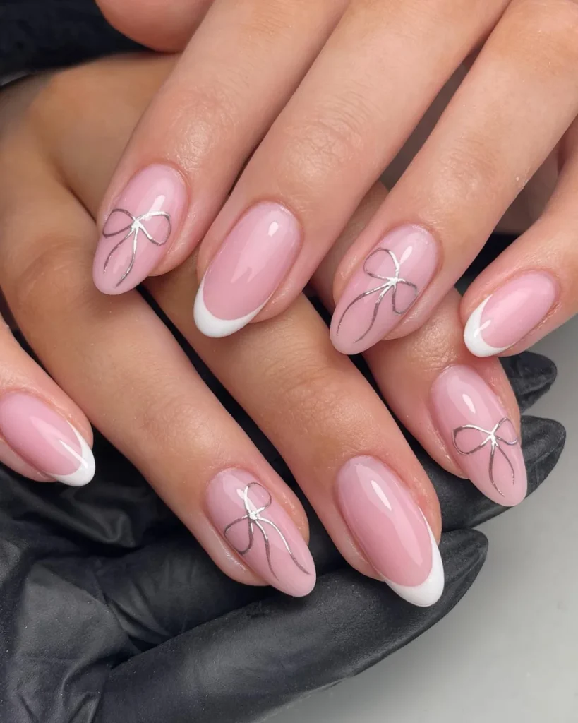 Short french tip christmas nail designs featuring glossy blush-pink almond nails, crisp white French tips, and delicate silver bow art, perfect for white french tip christmas nail designs inspiration.