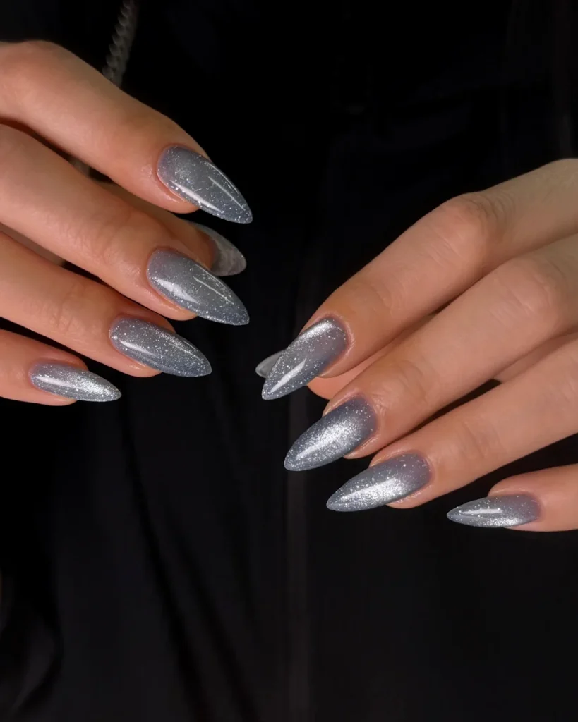 Silver glitter Christmas nail designs with shimmering metallic polish on long almond-shaped nails against a black background.