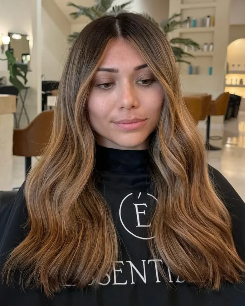 Warm honey brown balayage on dark brown hair with caramel highlights, golden brown tones, soft face-framing layers, and long, loose waves for a natural sun-kissed look