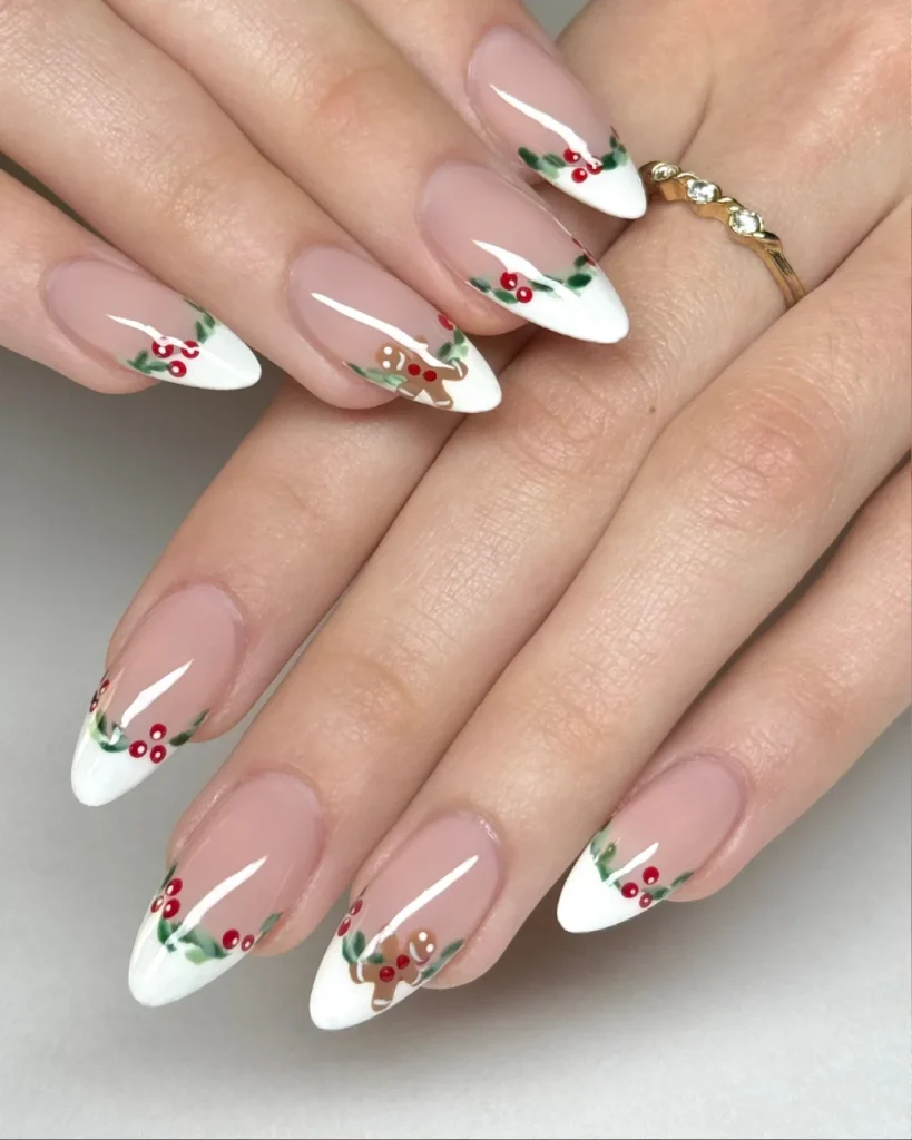 White french tip christmas nail designs with red holly berries, green leaves, and tiny gingerbread accents on a sheer pink base.