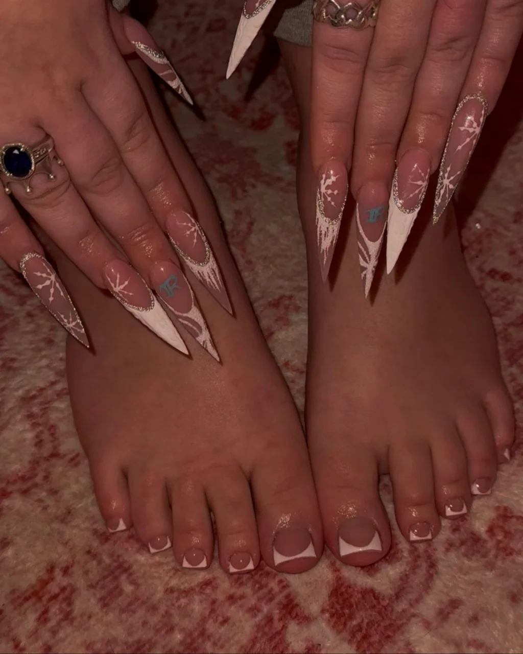 White french tip christmas nail designs with nude pink nails, pointed white tips, delicate snowflake art, and matching square French tip toenails.