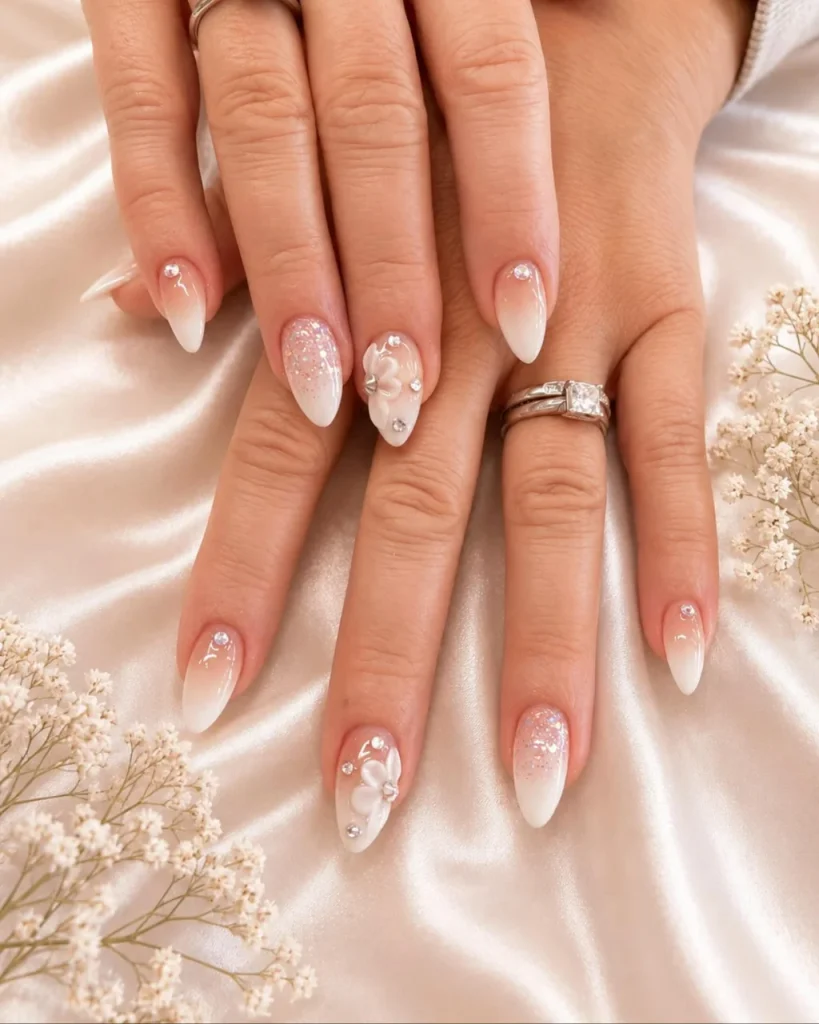 White French tip Christmas nail designs with sheer pink ombre, glitter, rhinestones, and 3D white floral accents.
