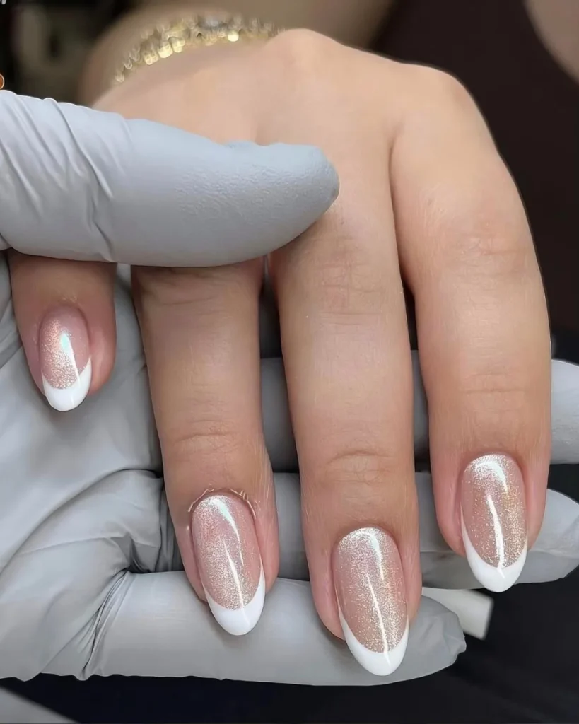 White french tip christmas nail designs with champagne-pink shimmer polish and elegant white tips on almond-shaped nails.