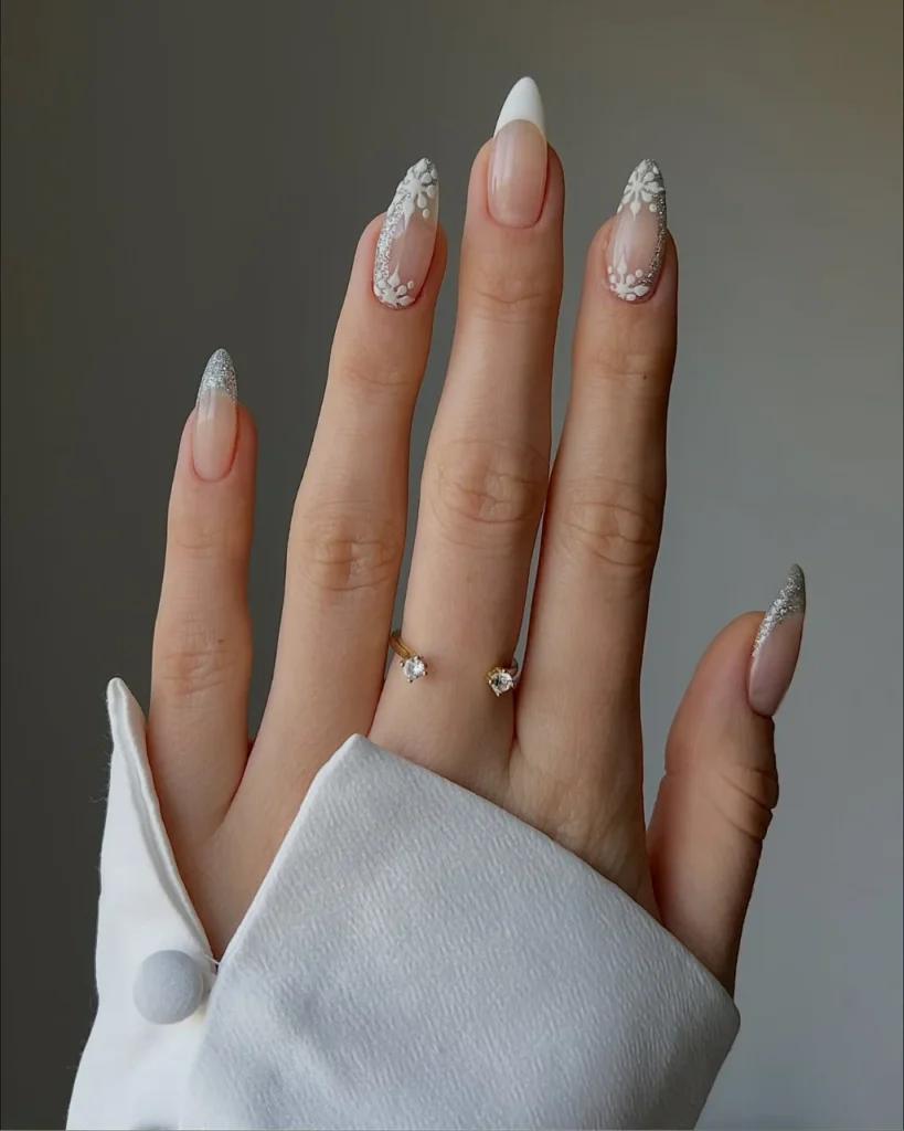 White french tip christmas nail designs with silver glitter tips and delicate white snowflake nail art on nude nails.